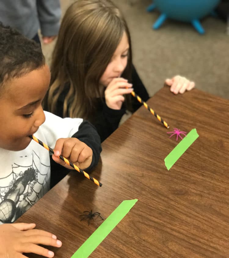 Students blow through straws for a Halloween spider race game.