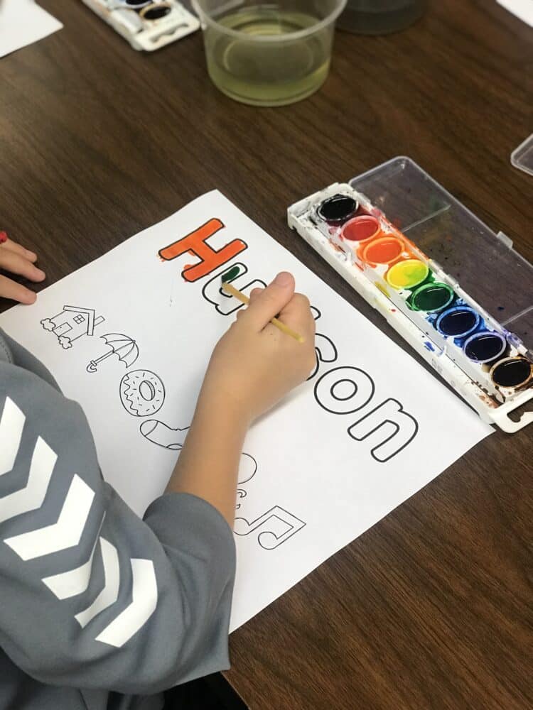 Student painting their name in letters and pictures with watercolor paints.